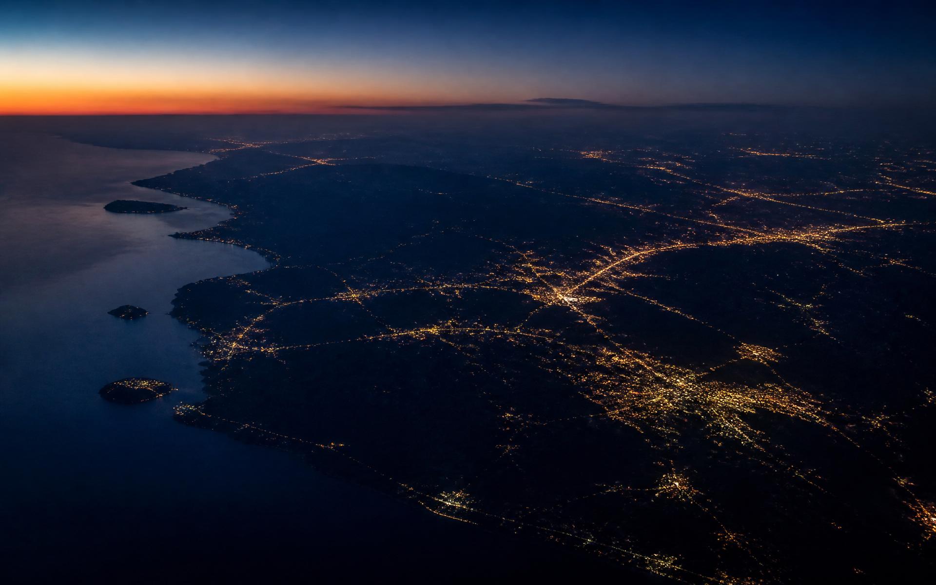 Aerial view of a continental coastline at dusk with distant city lights