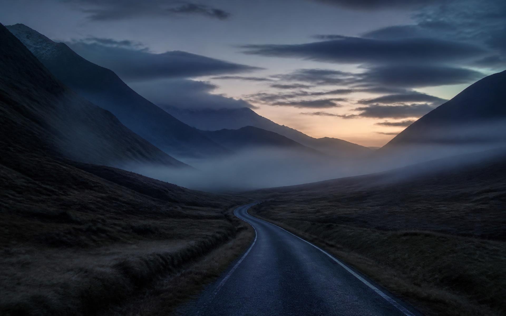 A single road curving through a misty valley at first light