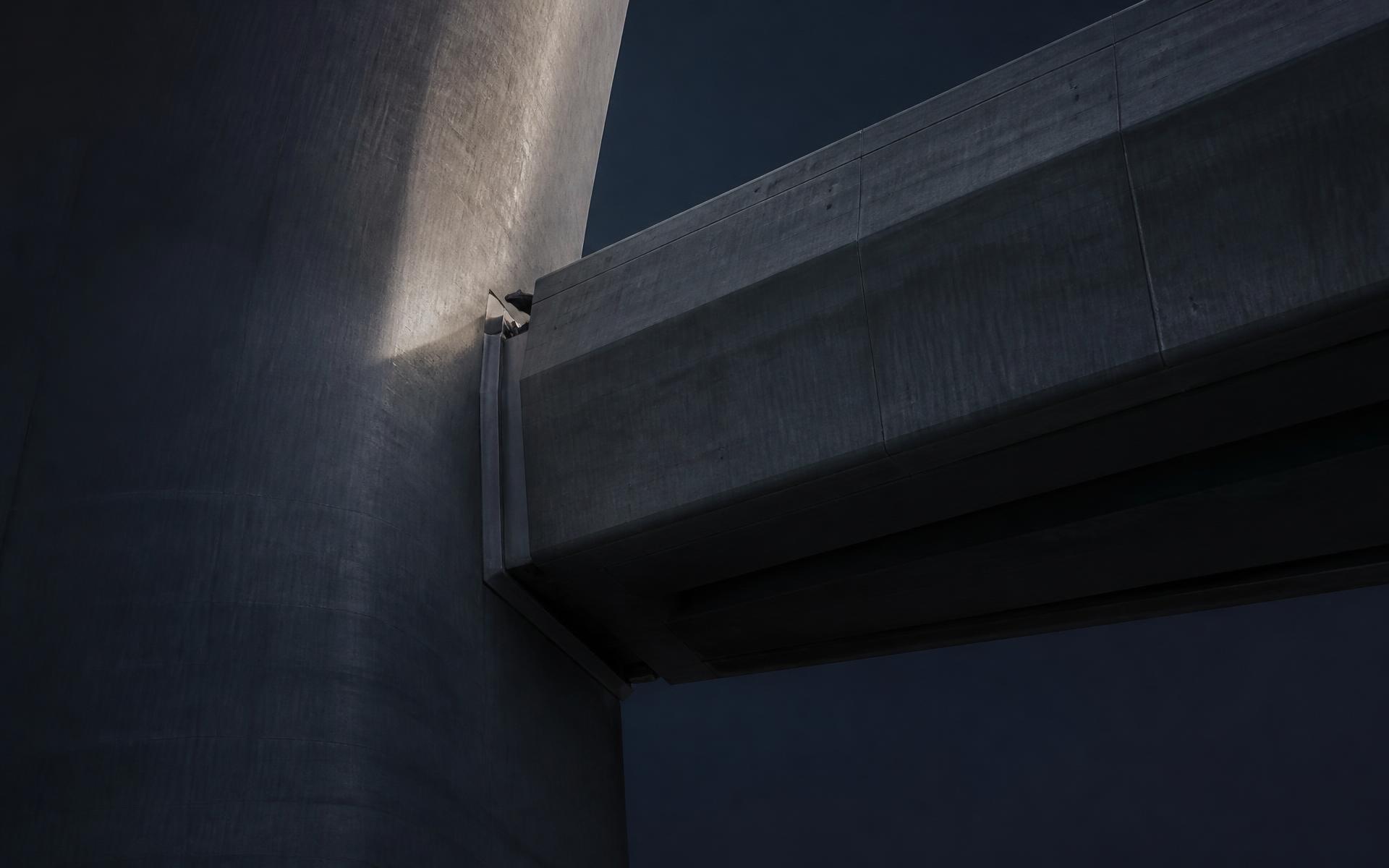 Two concrete volumes meeting at a structural joint under directional light