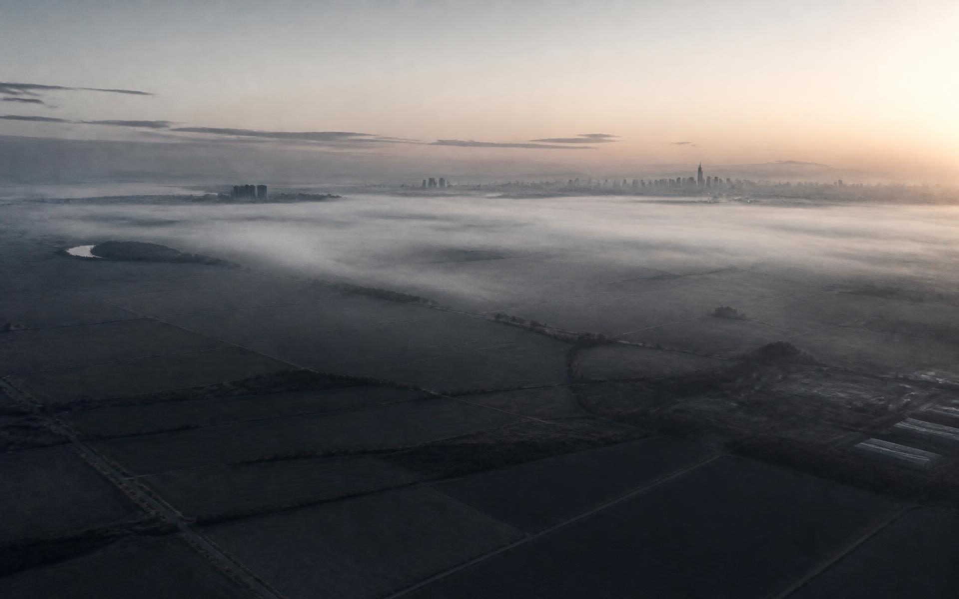 Aerial view of open land at dawn with a distant city skyline in mist